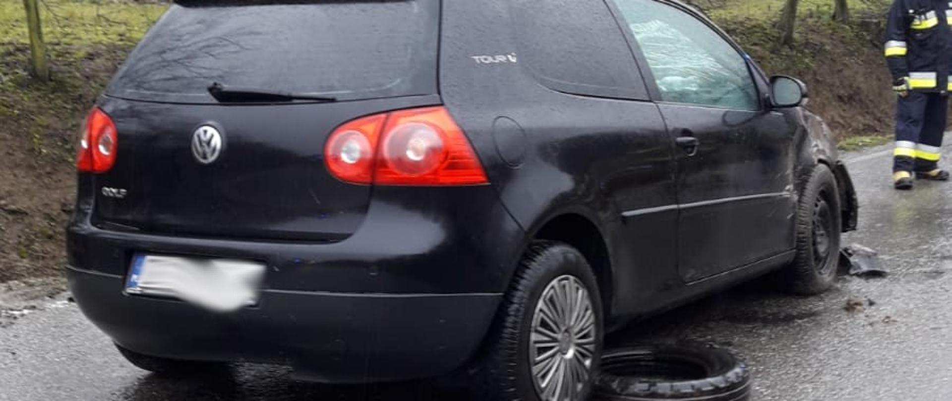 Samochód po dachowaniu stoi na kołach na drodze. W oddali stoi strażak.