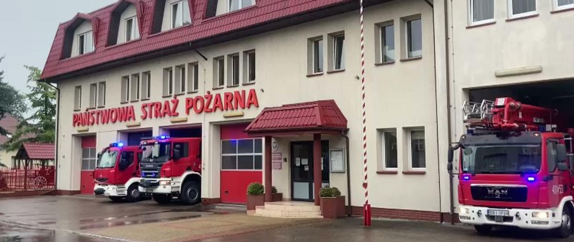 zdjęcie przedstawia trzy wozy ratowniczo gaśnicze przed garażami JRG w Bielsku Podlaskim z włączonymi światłami alarmowymi