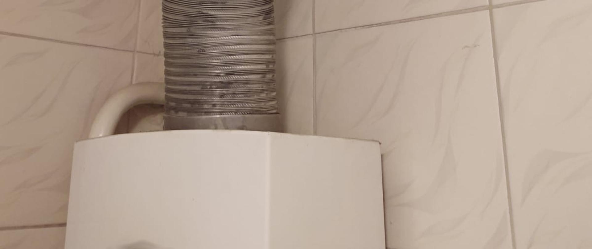 Fragment górny pieca gazowego do podgrzewania cieplej wody. Widoczna rura do odprowadzania sapalin.