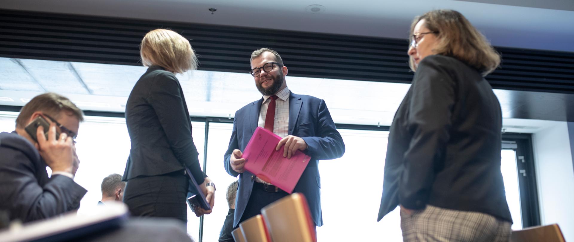 wiceminister Grzegorz Puda rozmawia stojąc z innymi uczestnikami spotkania, część uczestników już siedzi na krzesłach