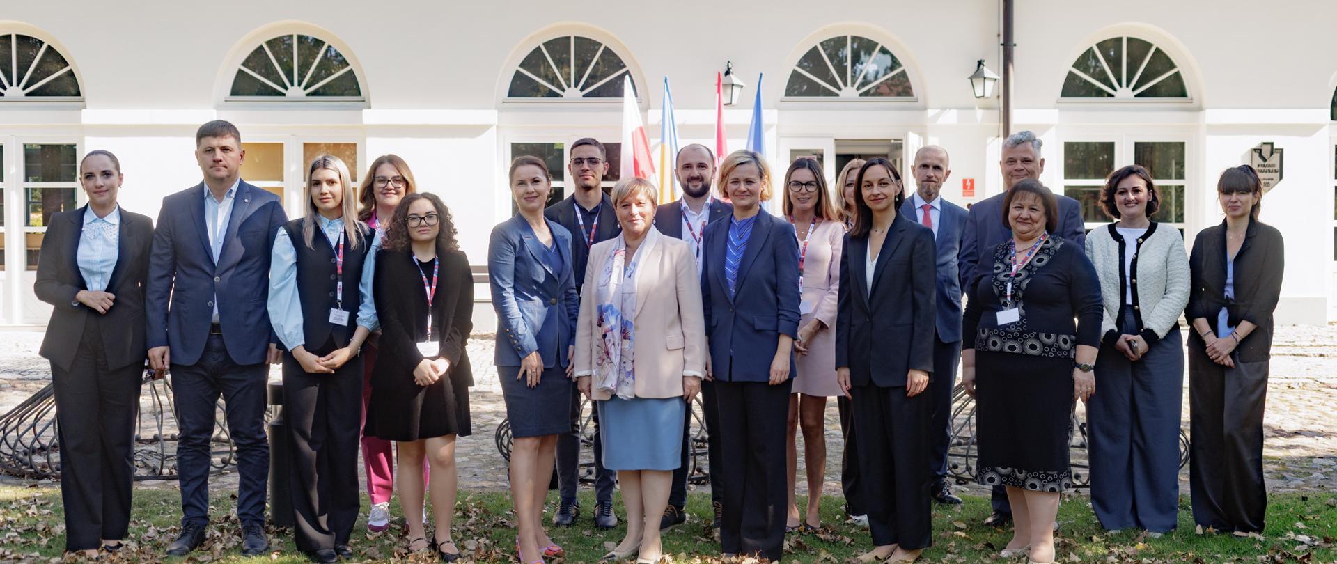 Dyrektor Zuzanna Kierzkowska, Zastępca Dyrektora Departamentu Współpracy Rozwojowej w Ministerstwie Spraw Zagranicznych i Olga Jabłońska, Zastępca Dyrektora Departamentu Współpracy Rozwojowej w Ministerstwie Spraw Zagranicznych pozują do zdjęcia w towarzystwie uczestników projektu PolTAC@Natolin przed budynkiem
