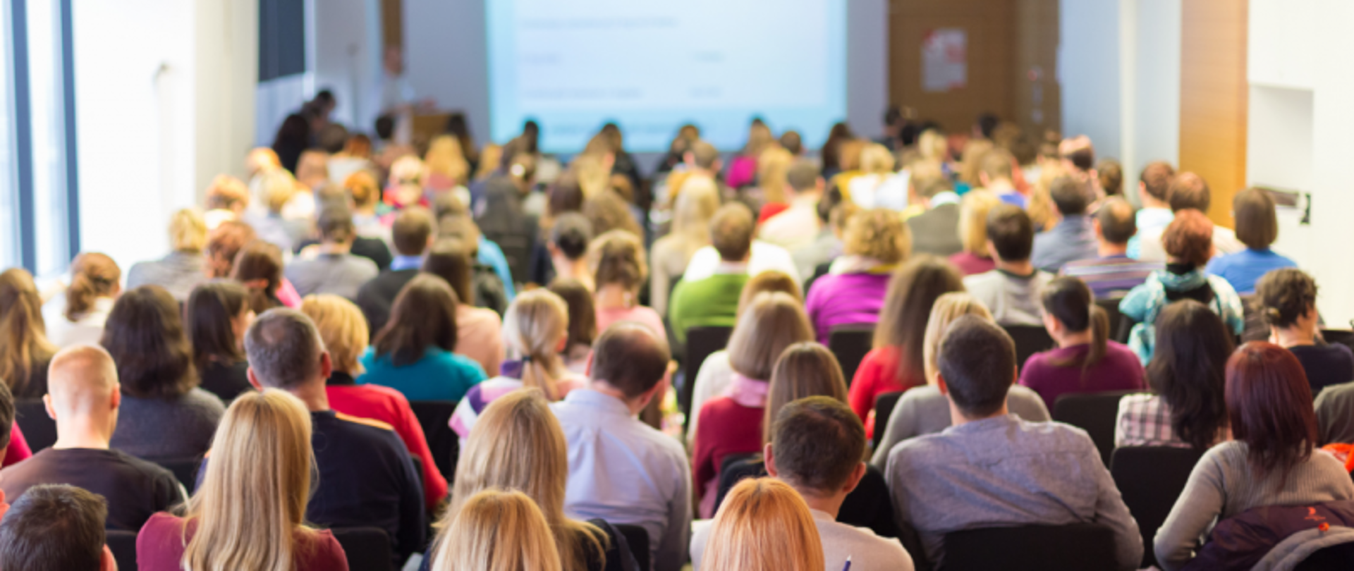 Widok sali konferencyjnej z publicznością zwróconą w stronę ekranu prezentacyjnego.
