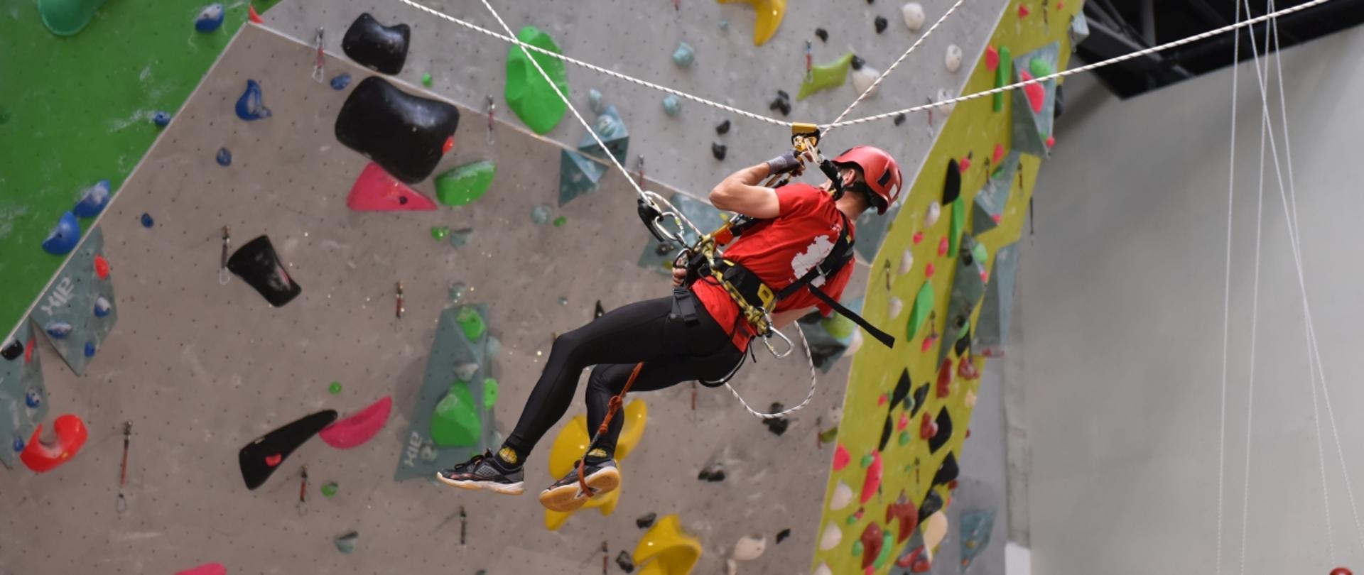 zawodnik poruszający się na linach w czasie zawodów w tle ścianka wspinaczkowa