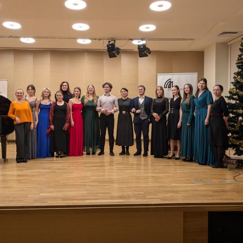 Zdjęcie przedstawia wspólne ujęcie wszystkich uczestników warsztatów wraz z prowadzącą i pedagogami na scenie sali koncertowej, w tle banery szkoły