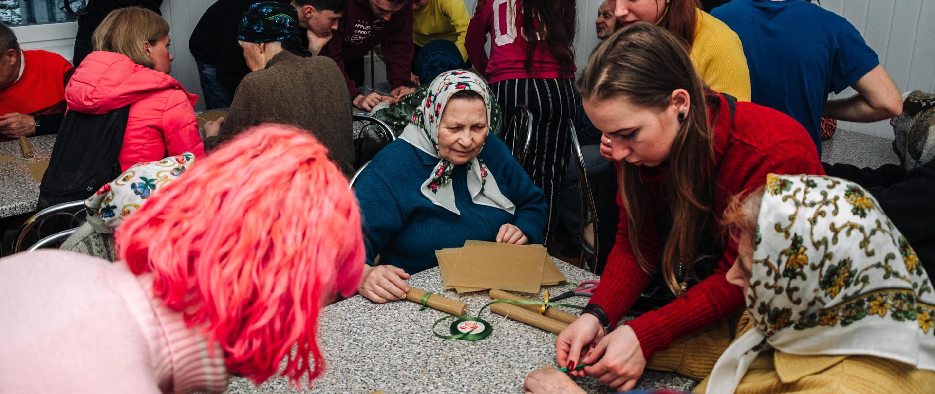 Grupa kilkunastu osób zajęta przygotowywaniem rulonów związanych zieloną wstążką.