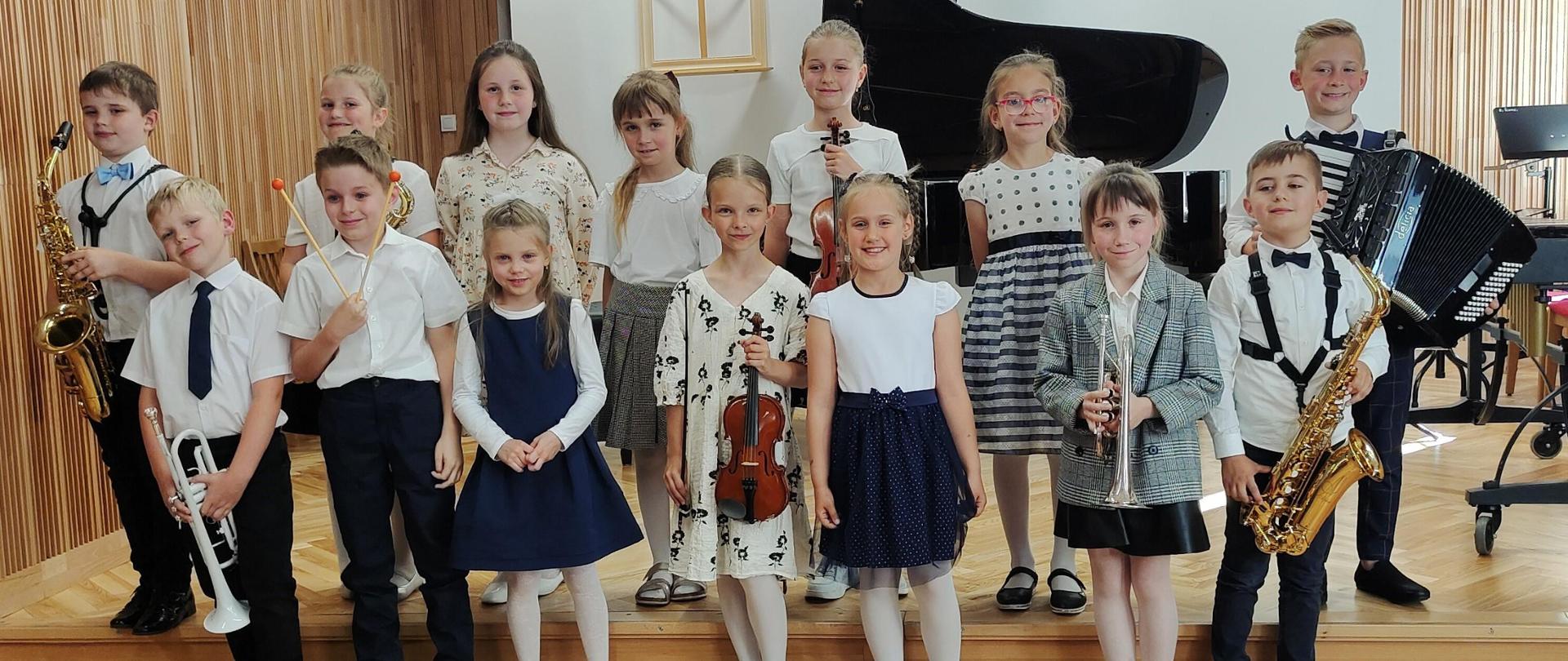 zdjęcie grupowe uczniów klasy I, stojących na schodach sceny ze swoimi instrumentami