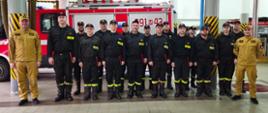 Zdjęcie grupowe na garażu jednostki ratowniczo-gaśniczej, stoi komendant wraz z awansowanymi i pozostałymi strażakami ze zmian służbowych.