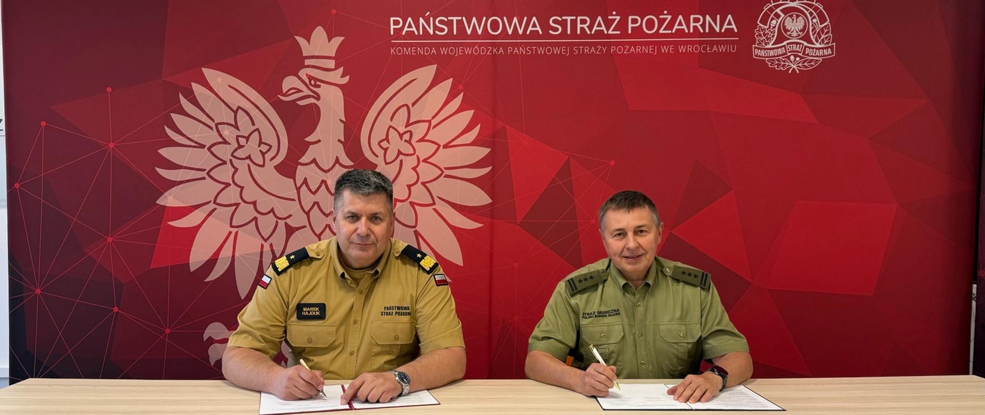 Zdjęcia przedstawiają dwóch mężczyzn w mundurach służbowych stojących lub siedzących przy biurku na tle czerwonej ścianki prasowej z napisem „Państwowa Straż Pożarna Komenda Wojewódzka Państwowej Straży Pożarnej we Wrocławiu” oraz godłem Polski. Mężczyźni podpisują dokumenty, trzymają teczki z umowami i wymieniają uścisk dłoni.