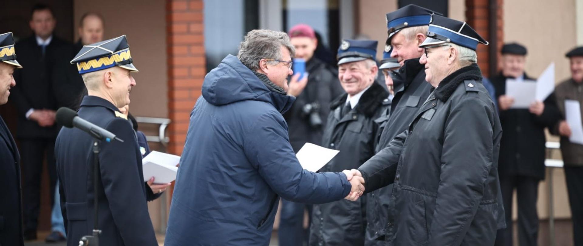 Wiceminister spraw wewnętrznych i administracji oraz komendant główny PSP wręczają druhom OSP decyzje o przyznaniu świadczenia ratowniczego 
