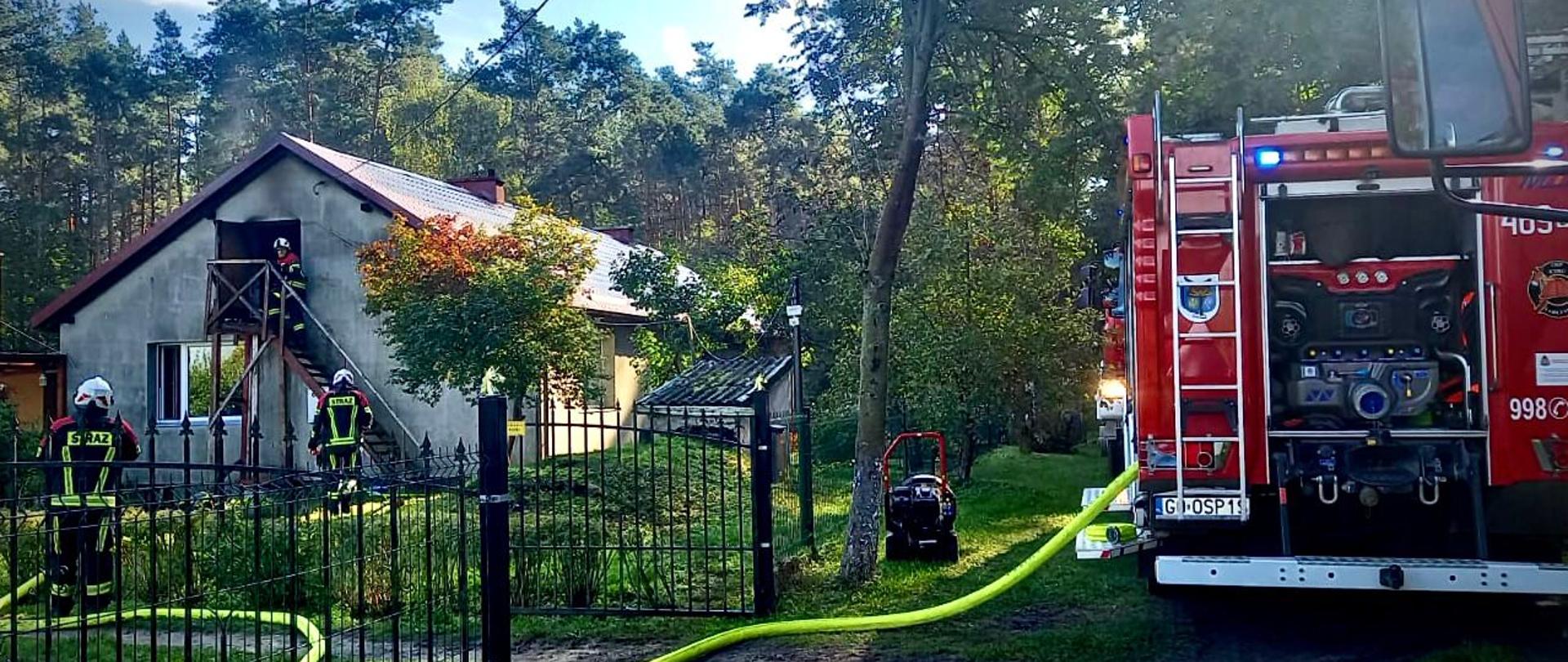 Pojazd ratowniczy stoi przed budynkiem mieszkalnym, strażacy wchodzą do obiektu