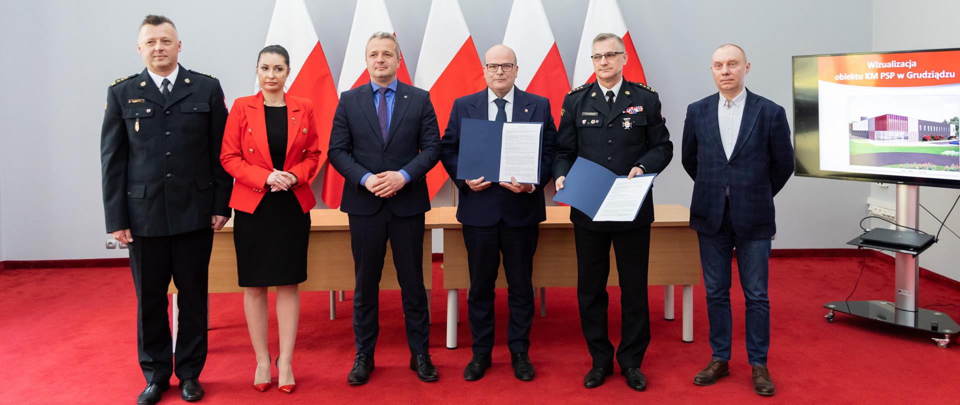 Jedna kobieta i pięciu mężczyzn stojący na tle flag