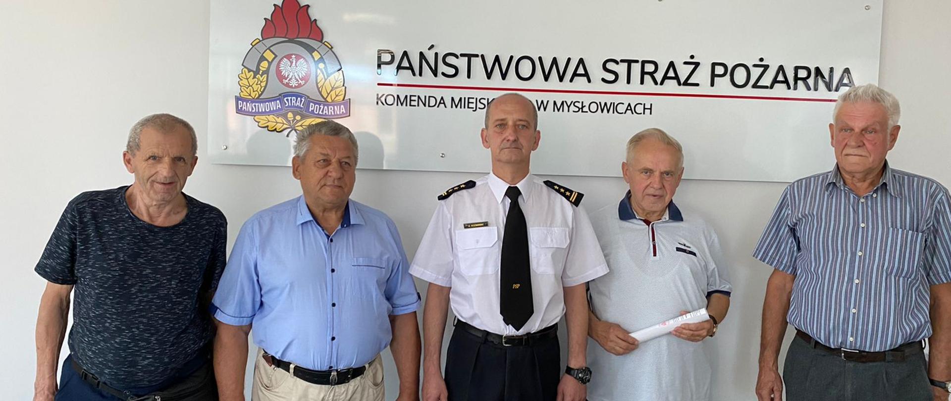 Zdjęcie przedstawia komendanta miejskiego PSP w Mysłowicach oraz druhów OSP którym przyznano świadczenie ratownicze. W tle logo PSP i napis Państwowa Straż Pożarna.
