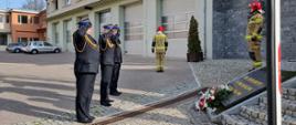 Kierownictwo Komendy Wojewódzkiej Państwowej Straży Pożarnej w Gdańsku oddaje honory, pod pomnikiem złożono wiązankę. Obok stoją strażacy w umundurowaniu specjalnym. 