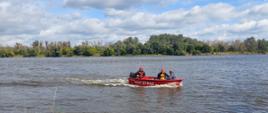 Zdjęcie przedstawia czerwoną łódź strażacką na rzece Wiśle. Na drugim planie tereny zielone