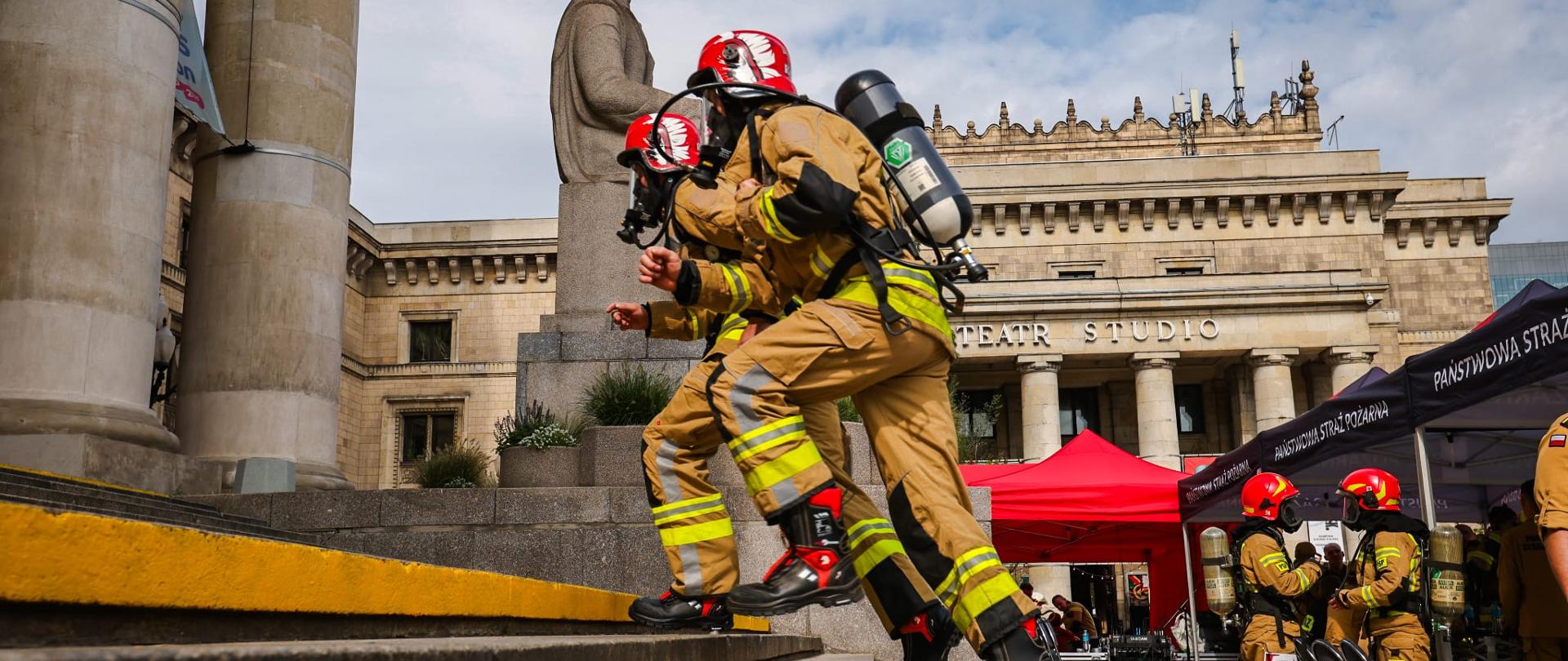 Strażacy w pełnym umundurowaniu wbiegają po schodach na Pałacu Kultury i Nauki.