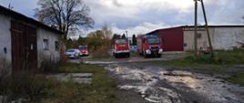 Zdjęcie przedstawia pojazdy pożarnicze na terenie w akcji gaśniczej odpadów zgromadzonych w hali magazynowej w Tucznie