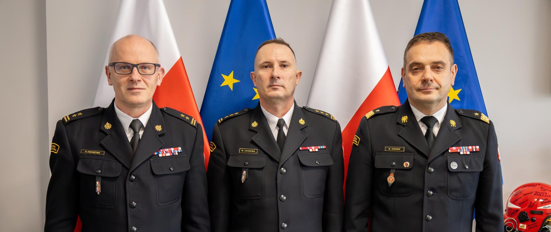 Na zdjęciu widzimy trzech strażaków w mundurach wyjściowych. Pozują do zdjęcia od lewej mężczyzna w okularach w stopniu brygadiera PSP, w środku mężczyzna w stopniu starszego brygadiera PSP, po prawej nadbrygadier PSP,