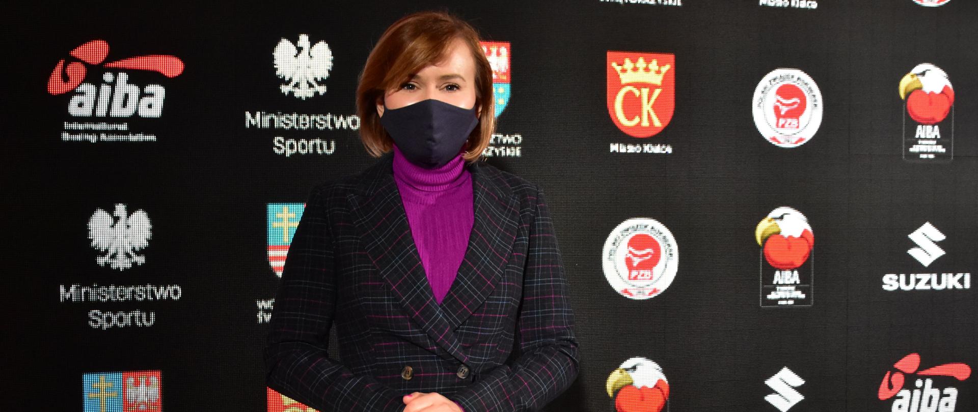 Sekretarz Stanu Anna Krupka podczas konferencji, w tle ścianka sponsorska.