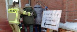 Druhna Ochotniczej Straży Pożarnej pomaga wejść po schodach starszej Pani do punktu szczepień. 