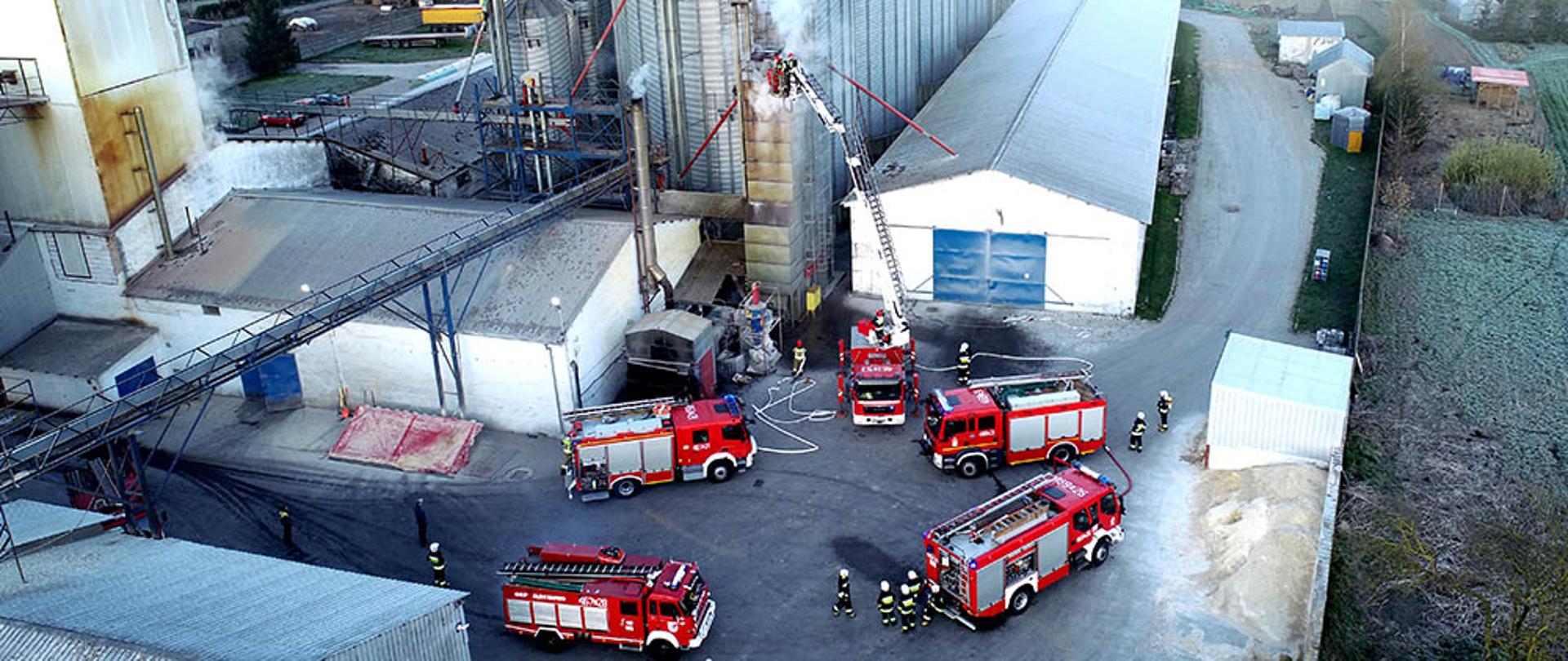 Zdjęcie przedstawia pożar suszarni, widok z lotu ptaka. na dole stoi 5 wozów strażackich które uczestniczą w akcji gaśniczej.