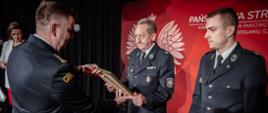 Strażacy ochotniczej straży pożarnej odbierają dyplomy okolicznościowe z okazji 30 lecia krajowego systemu ratowniczo-gaśniczego z rąk komendanta powiatowego na scenie