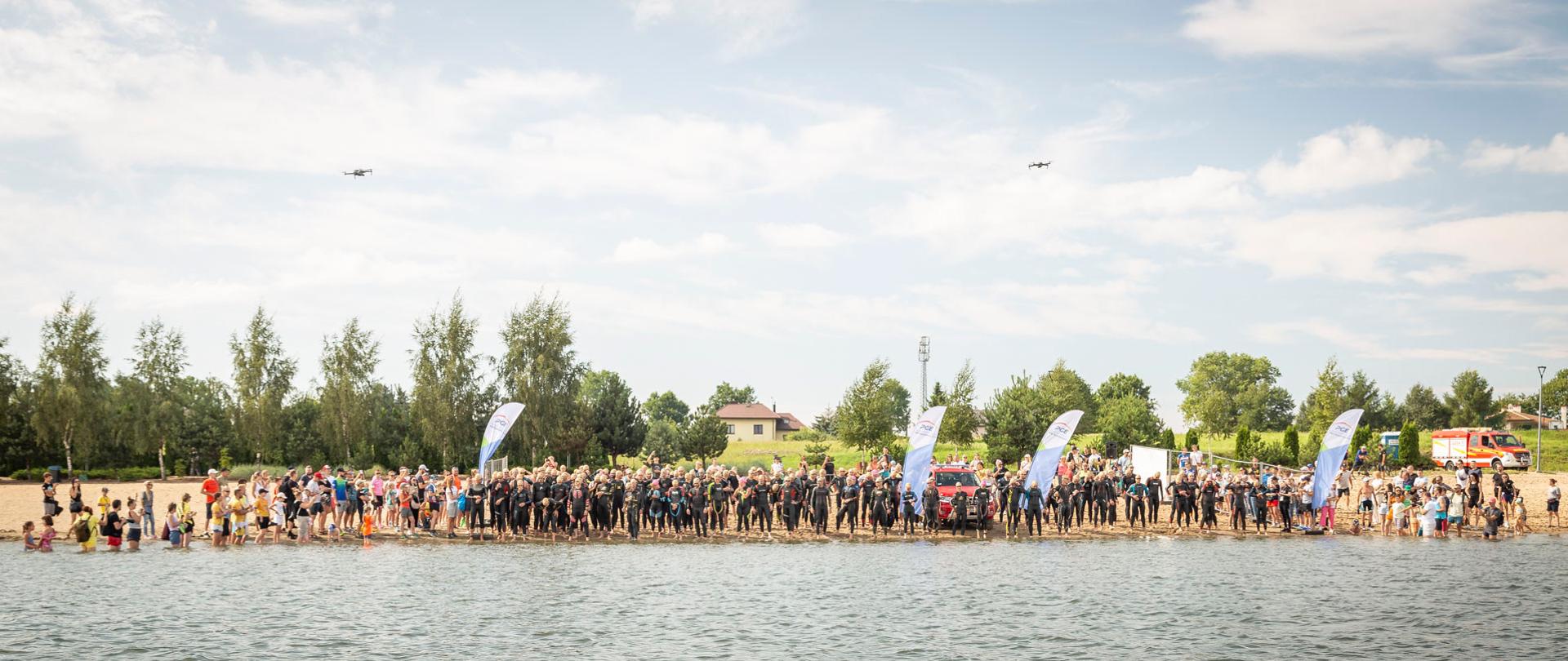 Grupa ubranych w stroje pływackie osób biegnie po plaży w kierunku wody