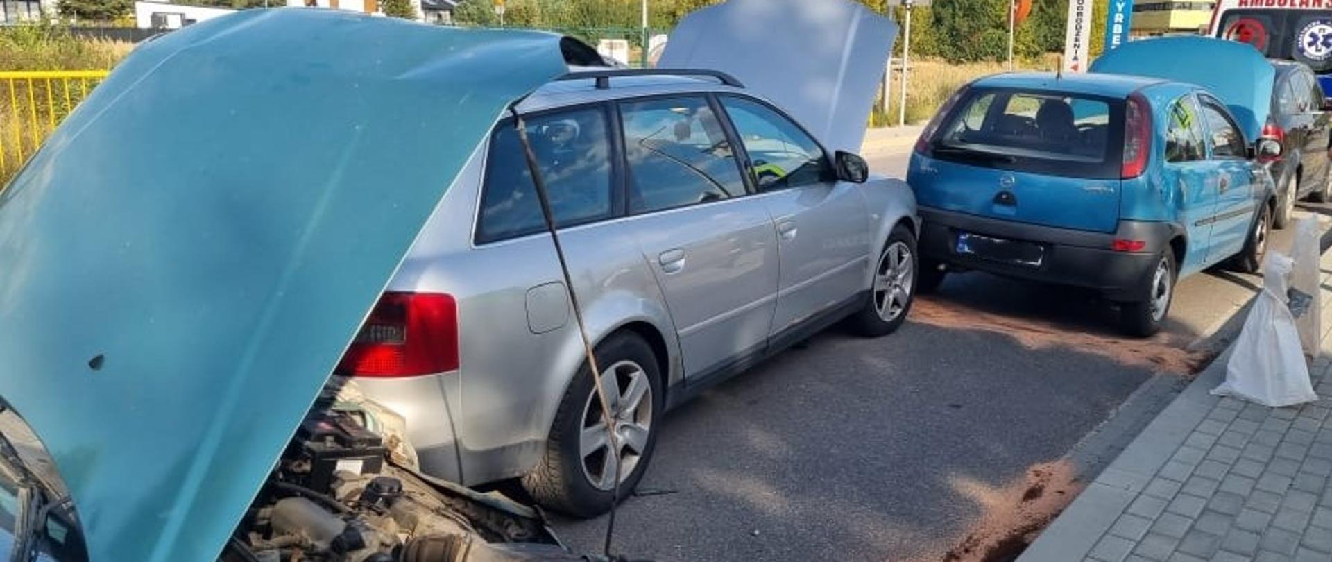 Zdjęcie przedstawia miejsce wypadku w Sukowie: na jednym pasie drogi stoją jeden za drugim 4 uszkodzone pojazdy, a w głębi widać fragment ambulansu Zespołu Ratownictwa Medycznego. Na jezdni rozsypany sorbent w celu usunięcia powstałych wycieków.