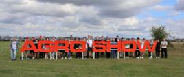 Grupa uczniów i nauczyciela zgromadzona za dużym czerwonym napisem AGRO SHOW