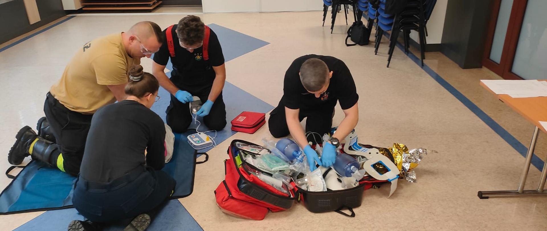 druhowie przystępują do podłączenia defibrylatora do manekina