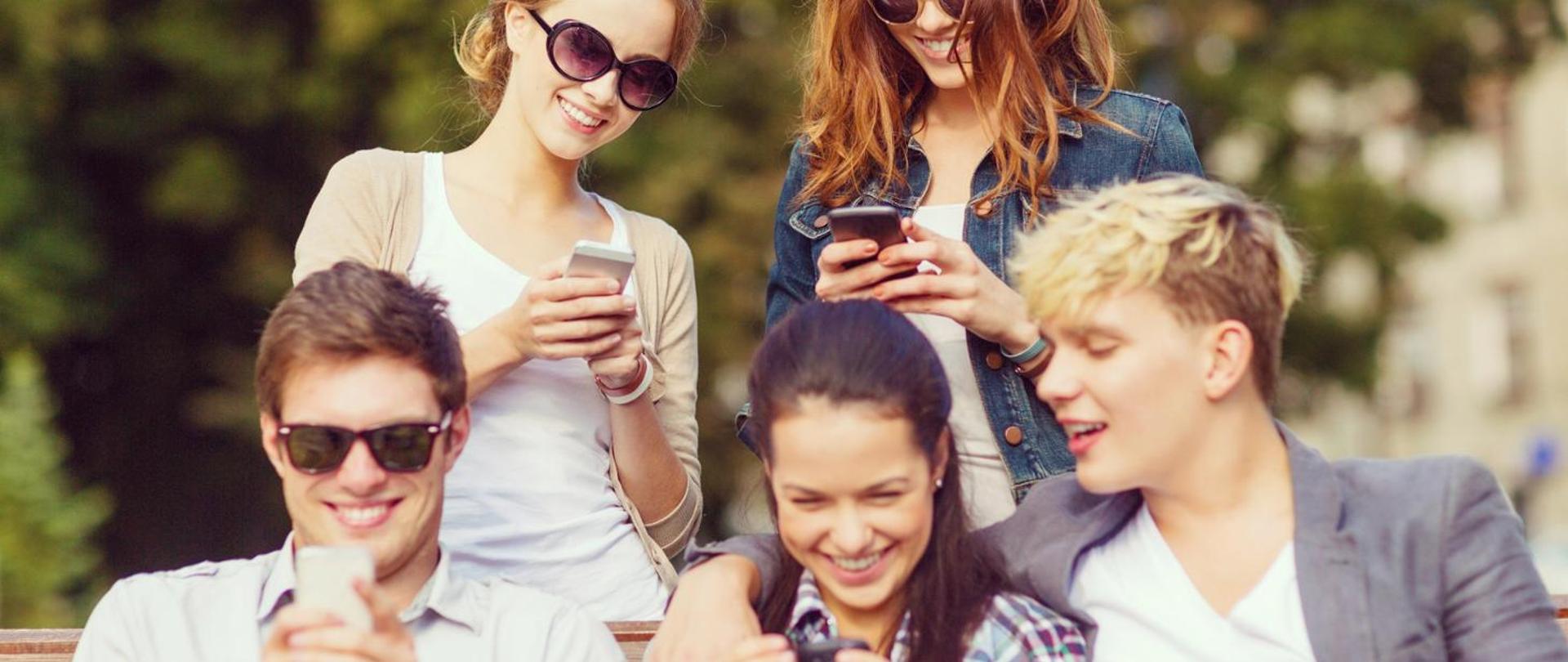 Zdjęcie przedstawia grupę młodych ludzi korzystających z aplikacji na telefonie