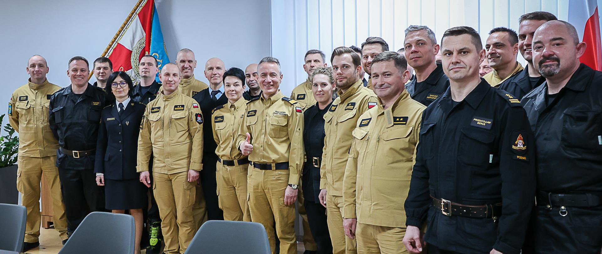 Na zdjęciu widać dwadzieścia pięć osób w gabinecie komendanta głównego PSP. W tle sztandar Komendy Głównej PSP.