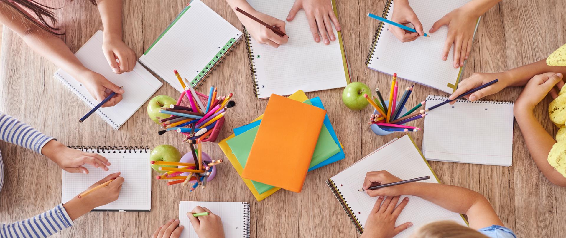 Uczniowie przy stoliku z kartkami, kredkami, jabłkami 