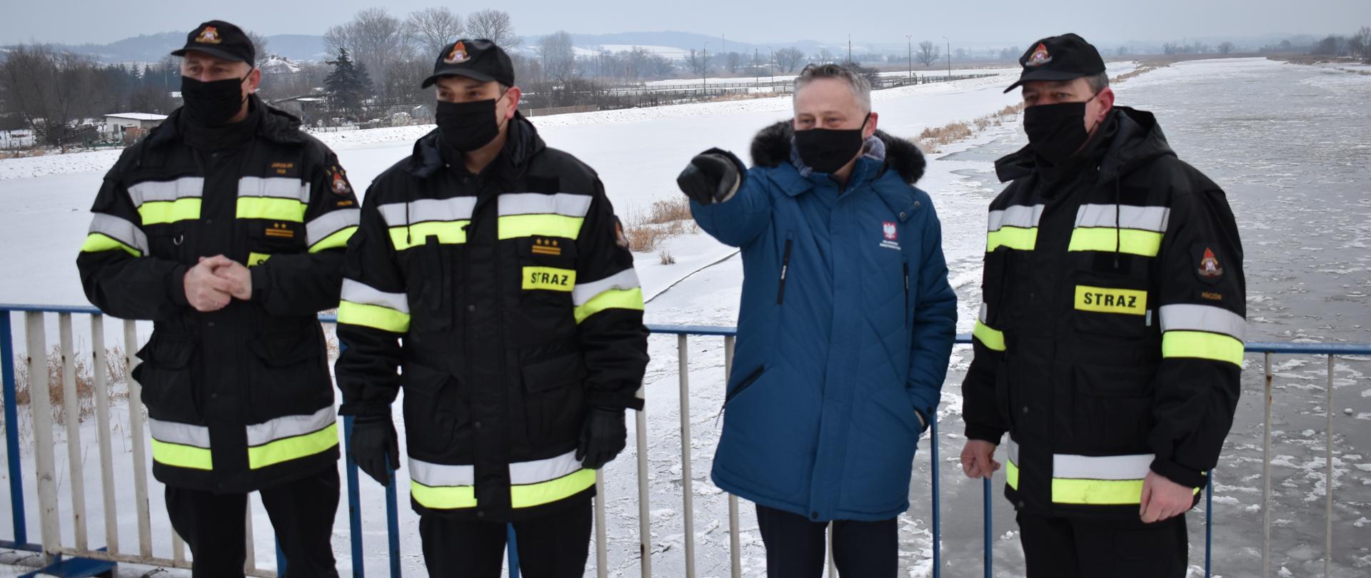 Na zdjęciu widać Wojewodę Świętokrzyskiego, Świętokrzyskiego Komendanta Wojewódzkiego PSP i kierownictwo pińczowskiej KP PSP podczas rozpoznania sytuacji hydrologicznej na rzece Nida. Ww. osoby znajdują się na moście na rzece Nida w Pińczowie. 