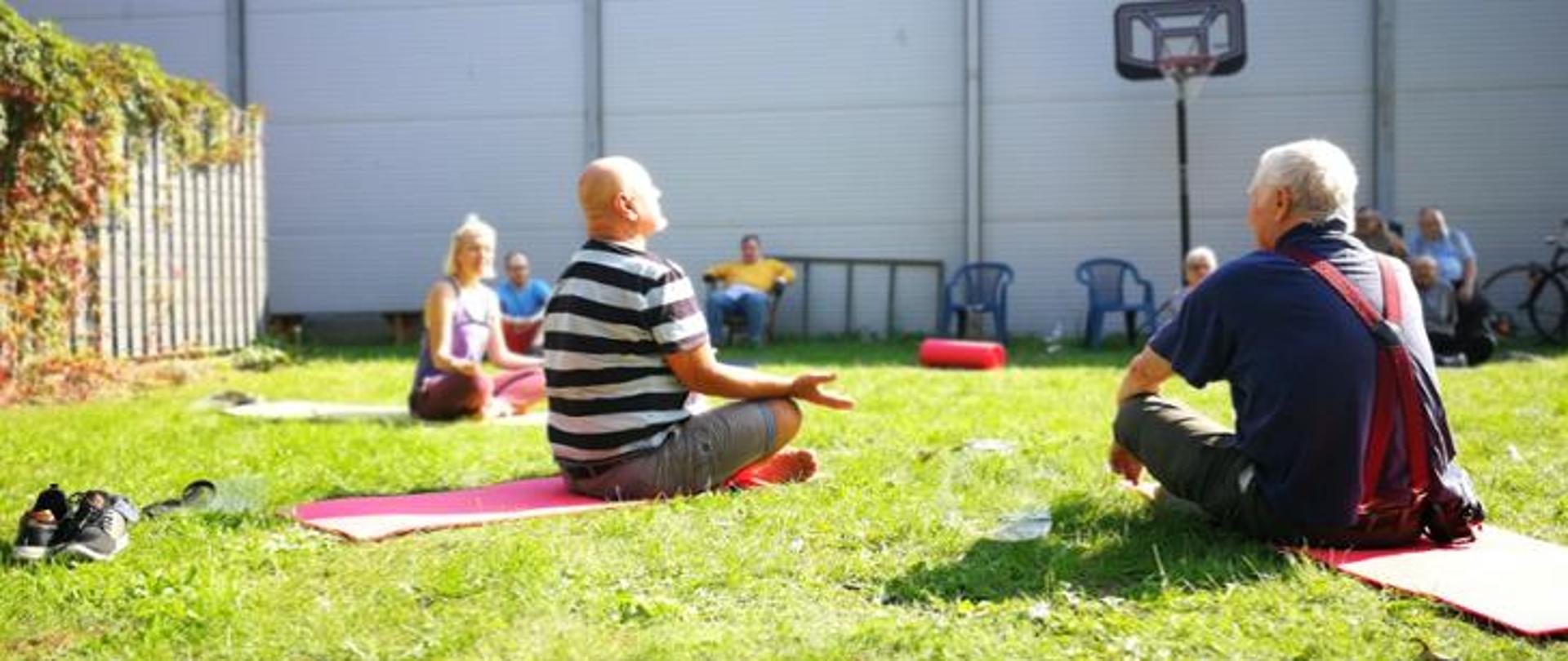 Uczestnicy środowiskowego domu samopomocy siedzą na trawie i biorą udział w zajęciach.