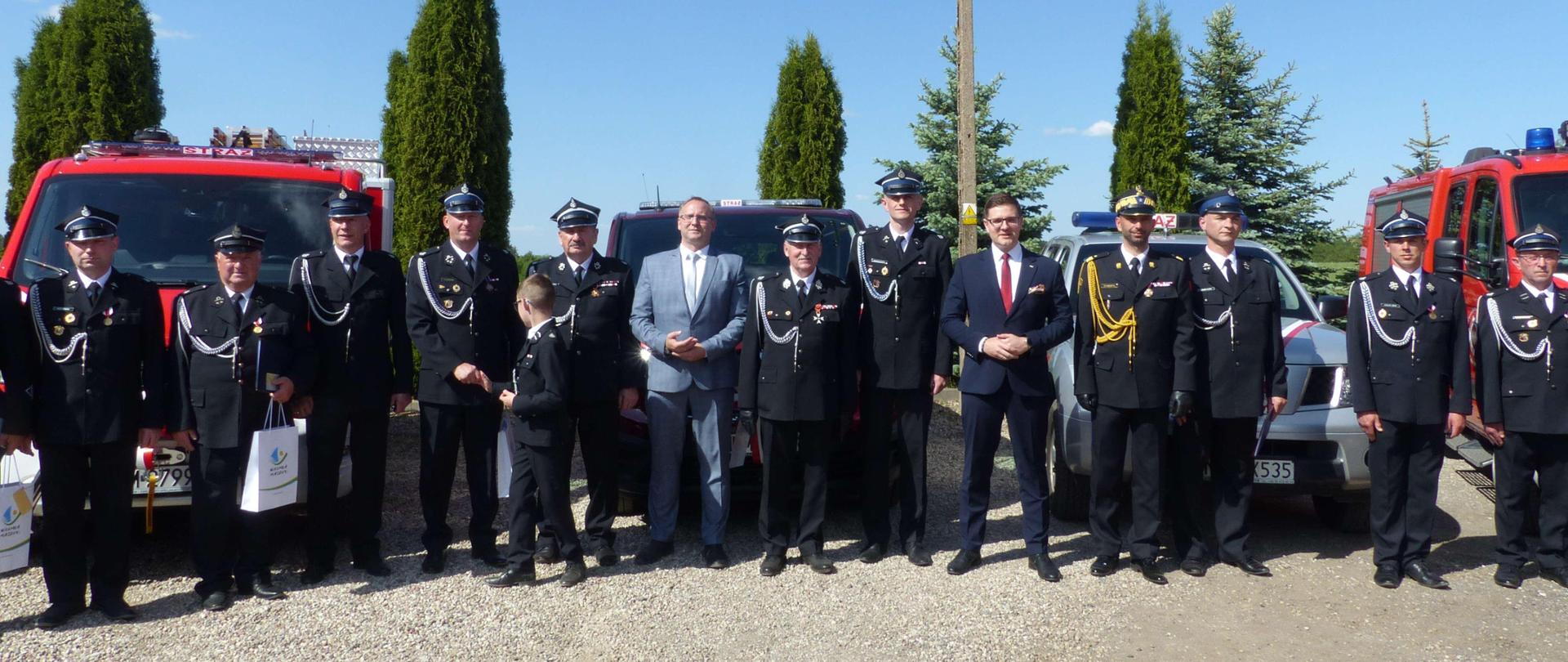 Zaproszeni goście i druhowie OSP na tle pojazdów pożarniczych
