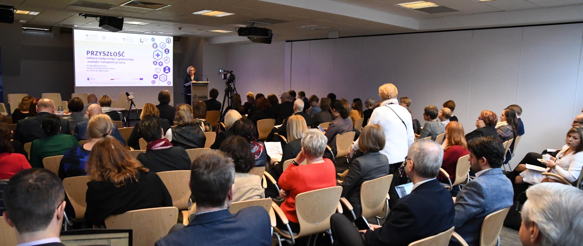 Sala konferencyjna wypełniona ludźmi słuchającymi przemówienia wiceminister Edukacji Narodowej – Marzeny Machałek