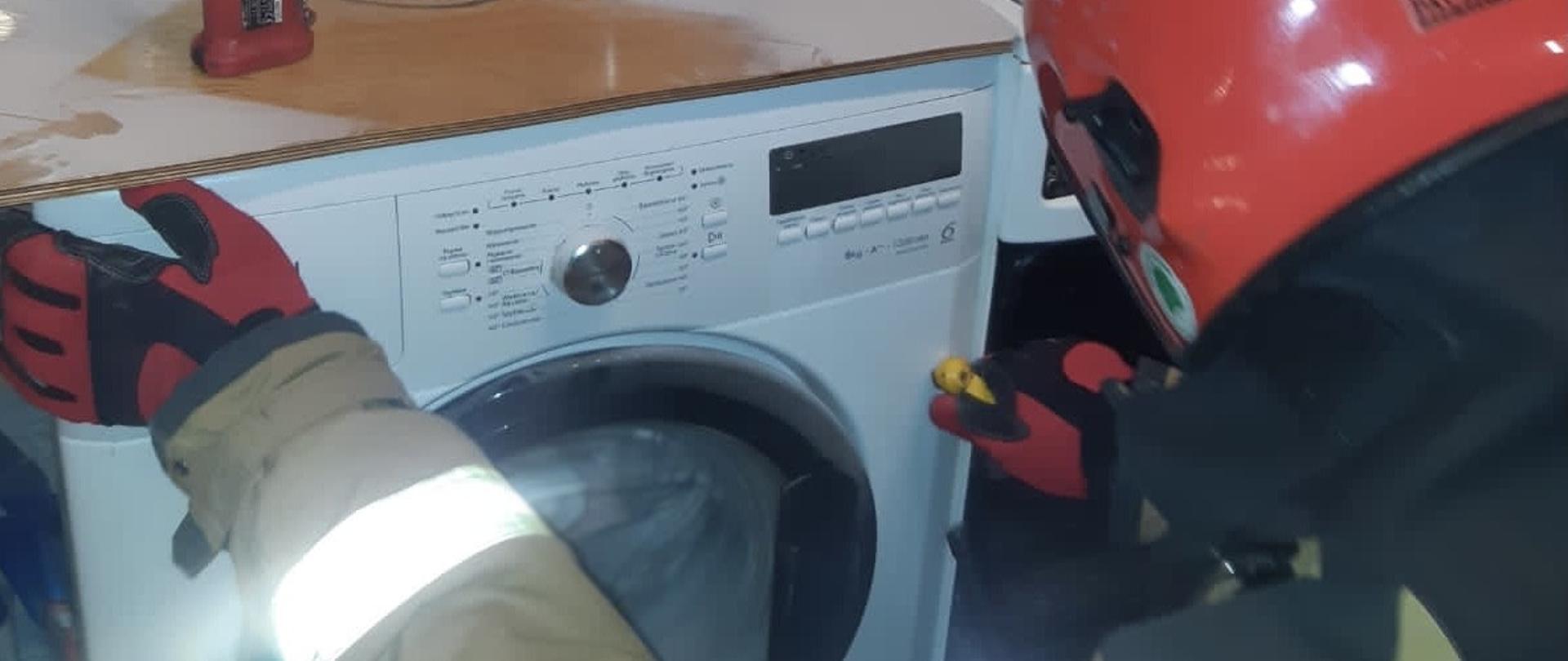 Strażak prowadzi czynności w kuchni przy pralce.