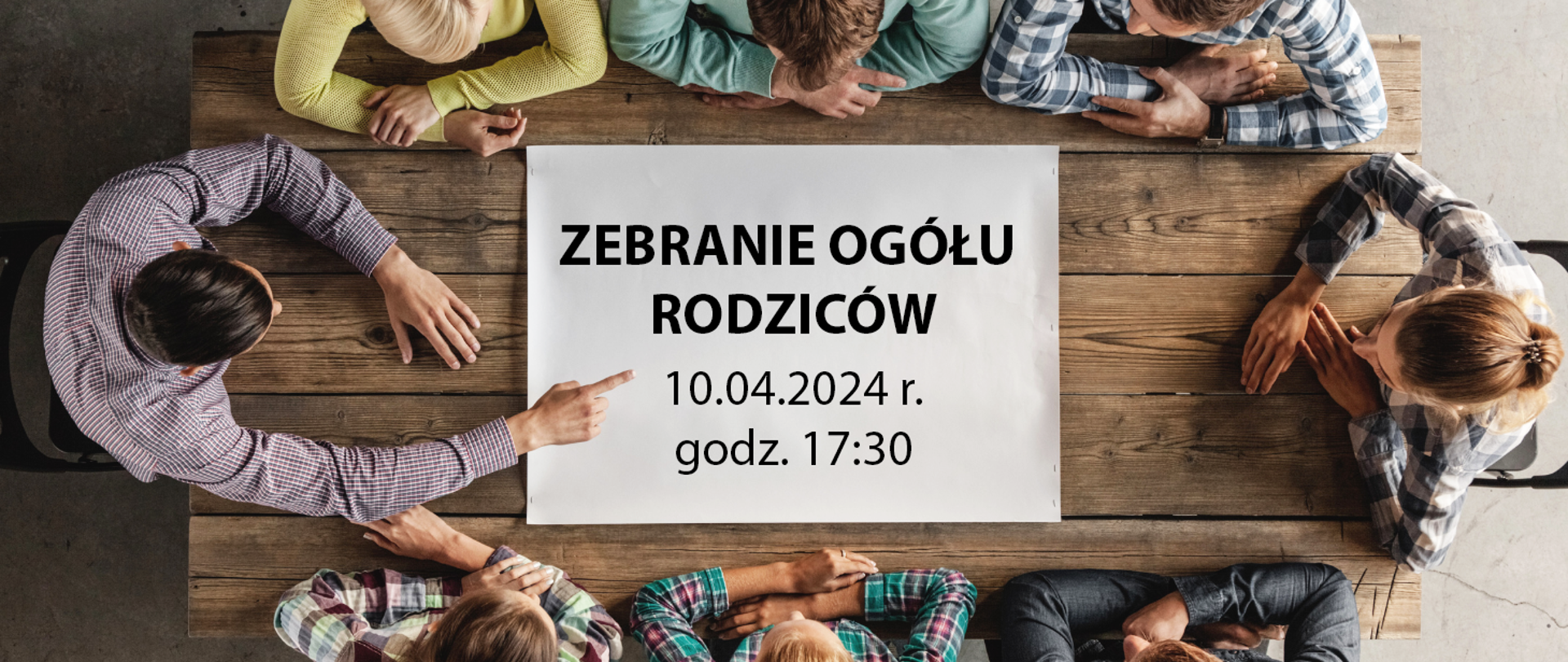 Baner przedstawia osoby siedzące i dyskutujące przy drewnianym stole (rzut z góry). Na środku owego stołu biała plansza z napisem "Zebranie ogółu rodziców 10.04.2024 r. godz. 17:30".