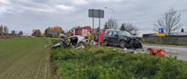 Na zdjęciu wypadek samochodowy (dwa rozbite samochody) w tle strażacy ratownicy medyczni pojazd pożarniczy oraz śmigłowiec LPR.
