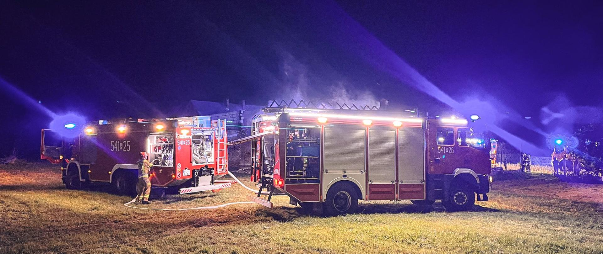 Samochody pożarnicze stoją przed zabudowaniami gospodarczymi, w których doszło do pożaru.