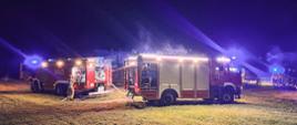 Samochody pożarnicze stoją przed zabudowaniami gospodarczymi, w których doszło do pożaru.