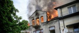 Na zdjęciu widoczni są strażacy podczas przygotowania do wejścia na koszyk drabiny mechanicznej, ubrani są w sprzęt ochrony dróg oddechowych aby podać prąd wody.