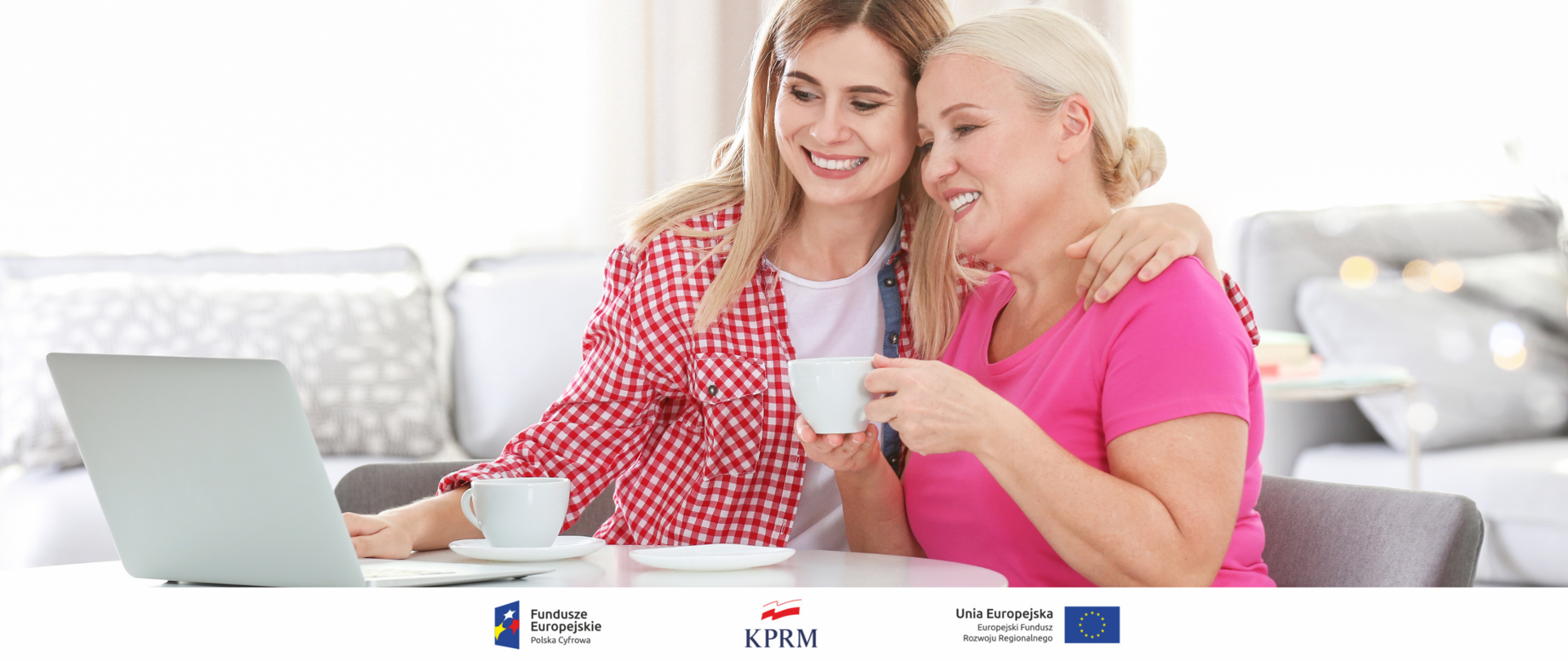 Zdjęcie - mama i córka siedzą przy stole i piją kawę, przed nimi biały laptop. Córka obejmuję mamę ramieniem, pokazując jednocześnie coś na ekranie laptopa.