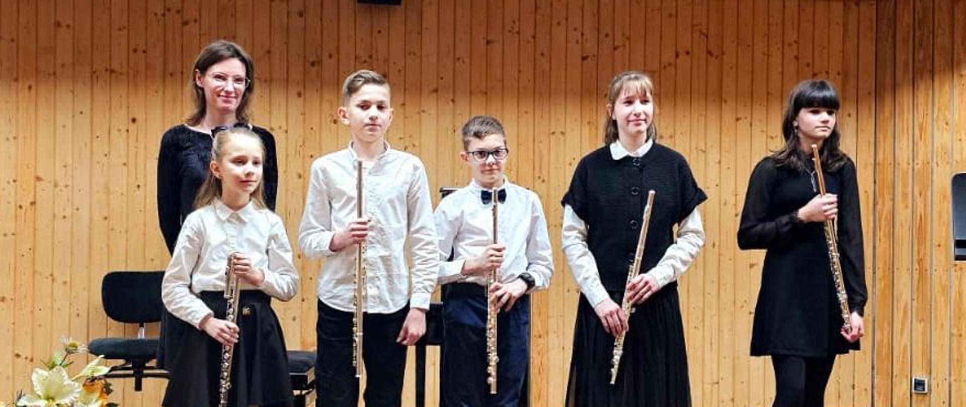 Na scenie stoją trzy dziewczyny i dwóch chłopców, za nimi stoi kobieta.