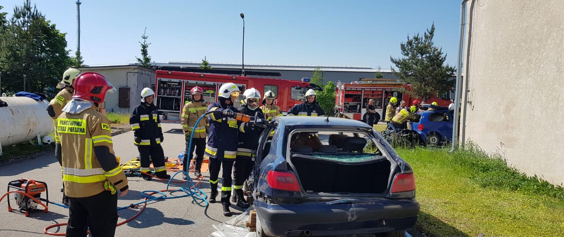 Na zdjęciu przedstawiono strażaków podczas przeprowadzonego kursu z zakresu ratownictwa technicznego. Po prawej stronie zdjęcia widać strażaków którzy za pomocą narzędzi hydraulicznych rozcinają karoserie samochodu osobowego.