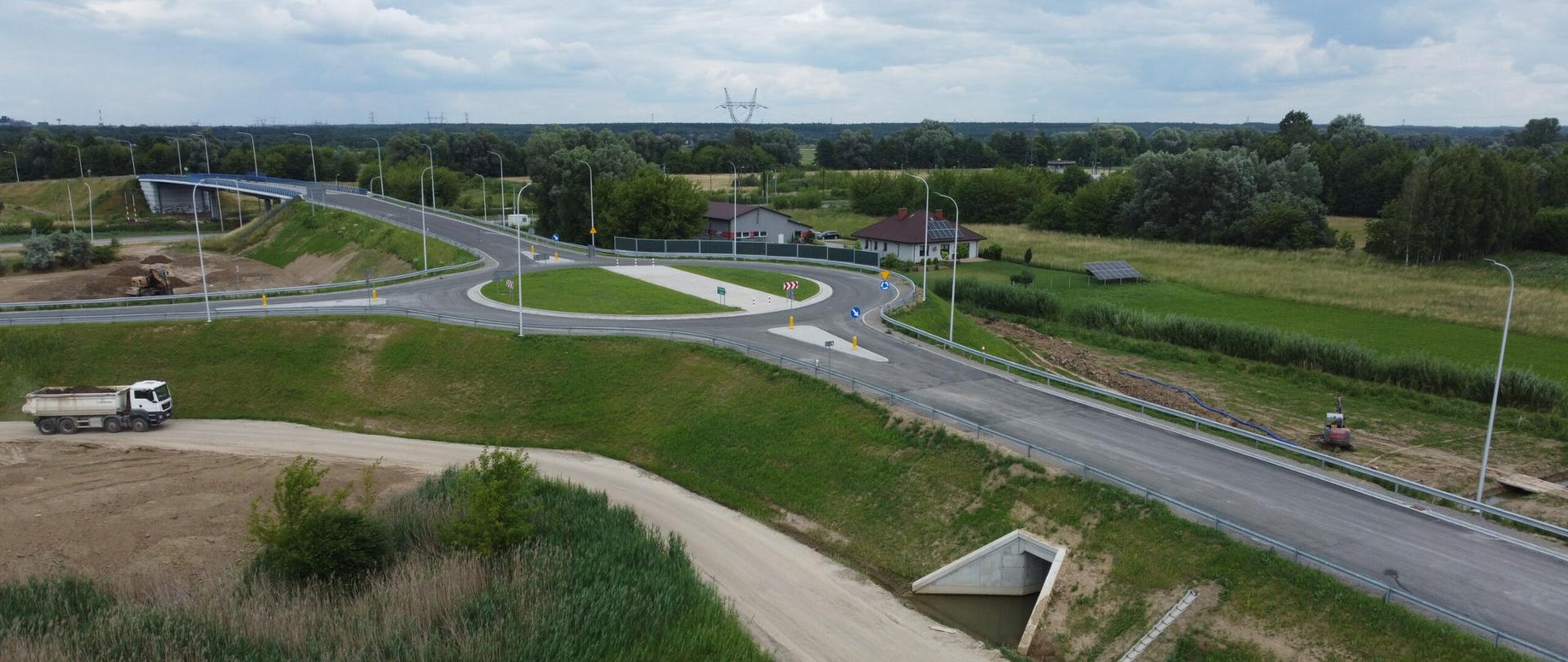 DK9 budowa obwodnicy Ostrowca Świętokrzyskiego - sfotografowany z góry węzeł z łącznicą, rondem na nasypie i wiaduktem nad drogą, dookoła zieleń 