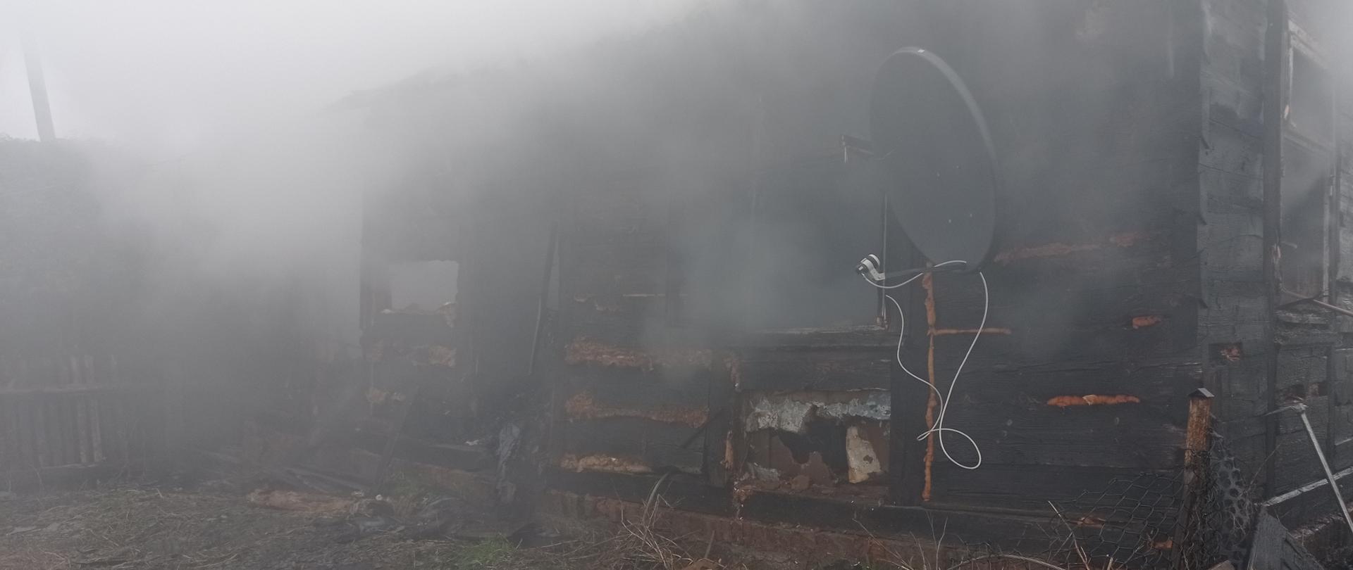 Front spalonego domu jednorodzinnego drewnianego. Z budynku wydobywa się dym