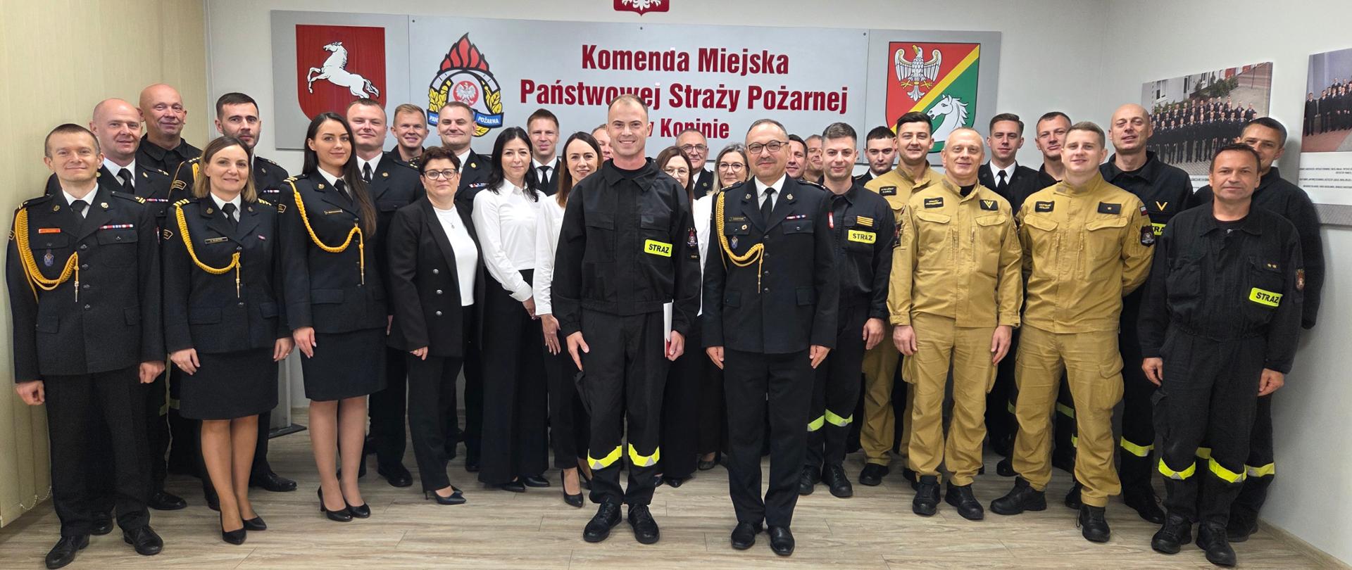 Funkcjonariusze oraz pracownicy cywilni komendy stoją w świetlicy podczas uroczystej zbiórki o okazji ślubowania nowego strażaka