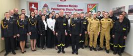 Funkcjonariusze oraz pracownicy cywilni komendy stoją w świetlicy podczas uroczystej zbiórki o okazji ślubowania nowego strażaka