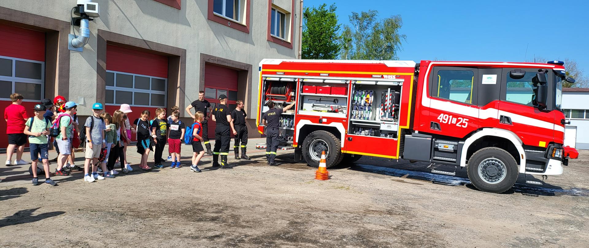 Zdjęcie przedstawia grupę szkolną , której strażacy JRG KP PSP Kłobuck pokazują wyposażenie samochodu pożarniczego